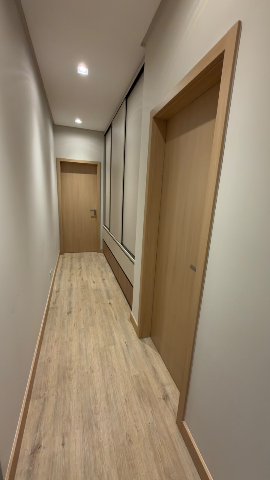 Corredor com portas amadeiradas, piso amadeirado e rodapé no mesmo tom