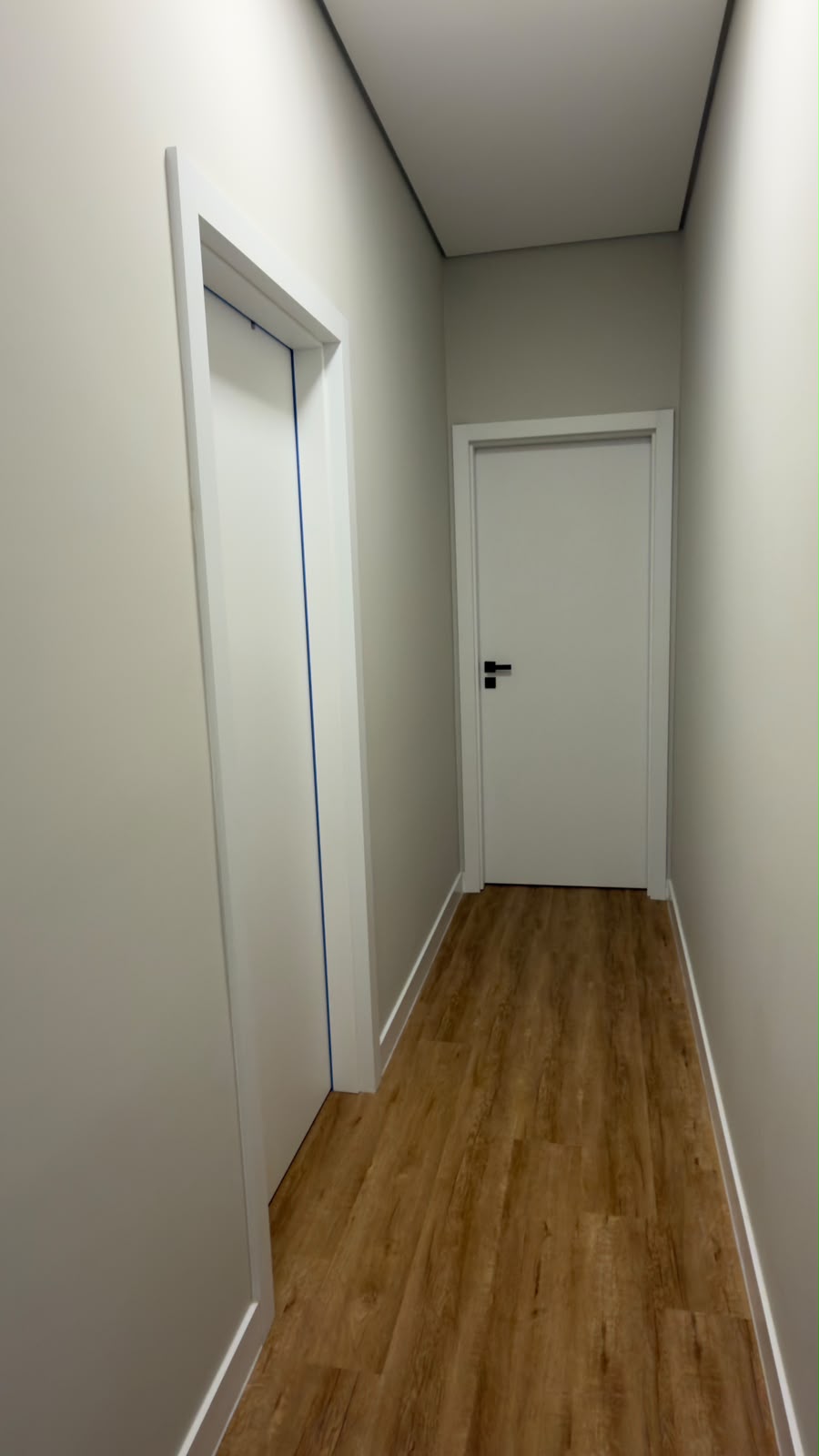 Corredor longo com portas brancas, piso amadeirado e rodapé branco