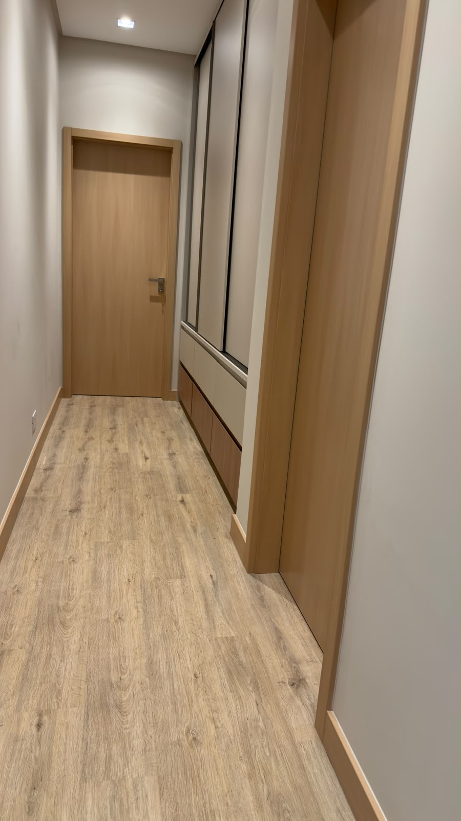 Corredor com portas amadeiradas, piso amadeirado e rodapé no mesmo tom