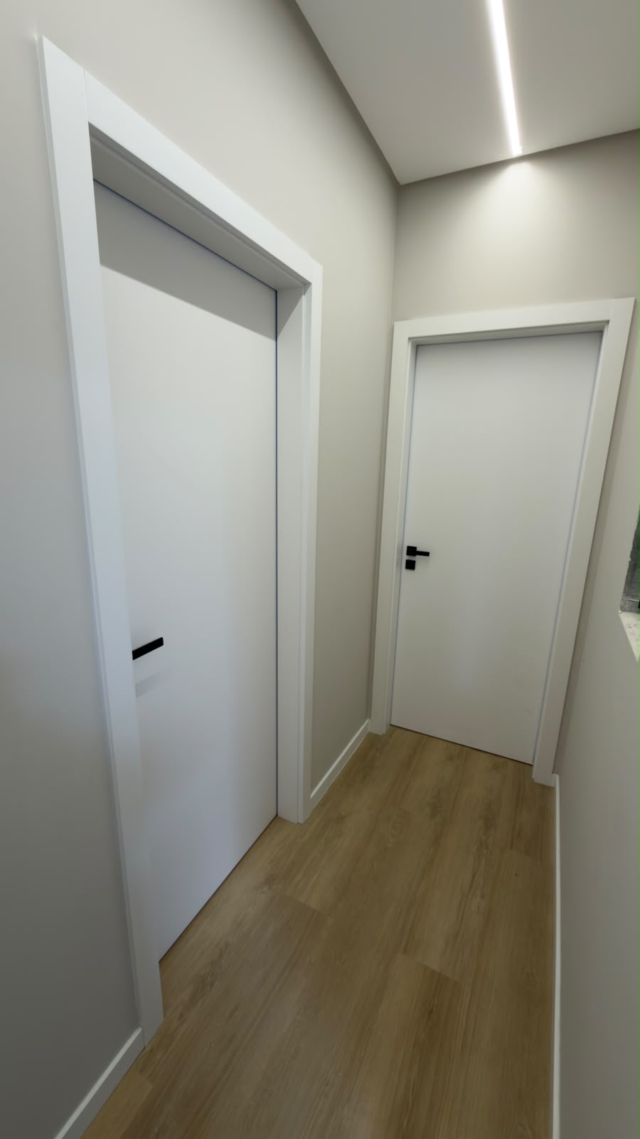 Portas brancas com puxadores pretos e piso amadeirado