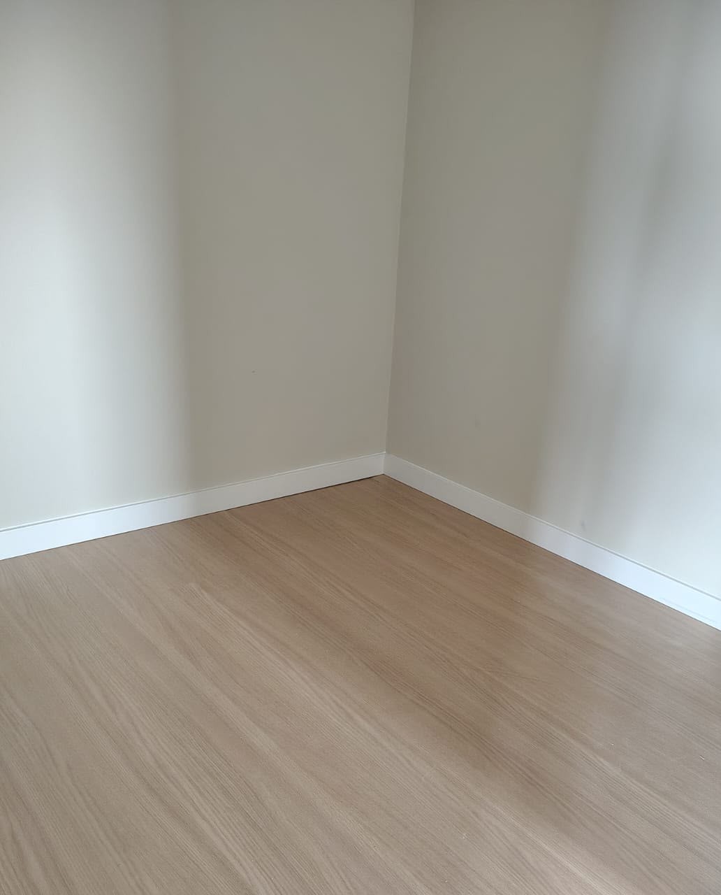 Canto de um quarto com rodapé branco e piso amadeirado claro